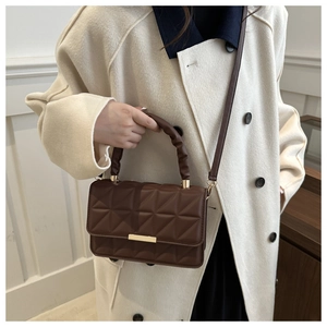 Detailed view of a brown quilted leather handbag with gold metal clasp on a beige coat