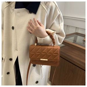 Detail of brown quilted leather handbag with gold clasp and gathered handle on model