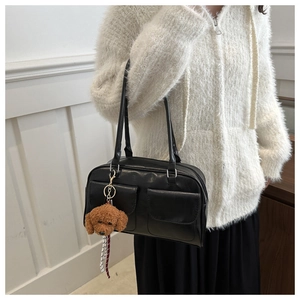 Détail du sac sous le bras en cuir noir avec poches à rabat et breloque ours en peluche