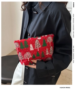Détail d'une pochette de Noël rouge avec motifs de sapins scintillants portée par un mannequin