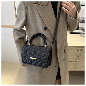 Detail of black quilted bag featuring gold metal clasp and ruched designer handle