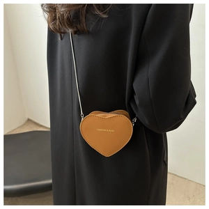 Brown heart-shaped leather crossbody bag with chain strap styled on a black coat