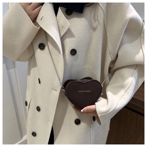 Detail of a dark brown heart-shaped mini bag with a silver chain strap on a wool coat