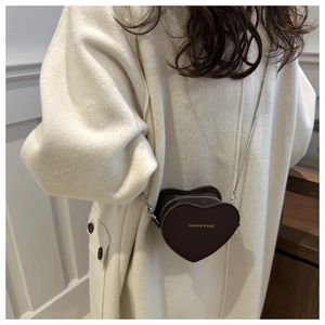 Detail of a dark brown heart-shaped mini crossbody bag with a fine silver metal chain strap