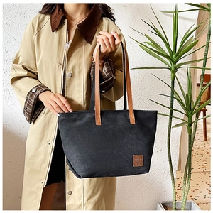 Détail du sac cabas en toile noire montrant les anses marron et le patch du logo