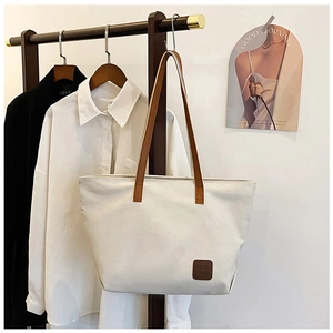 Détail du sac cabas en toile avec écusson logo en cuir marron et anses sur support