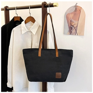 Gros plan d'un sac cabas en toile noire avec des anses en cuir marron sur un portant