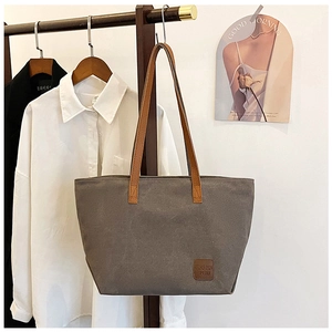 Détail d'un sac cabas en toile grise avec anses en cuir marron et patch logo rond