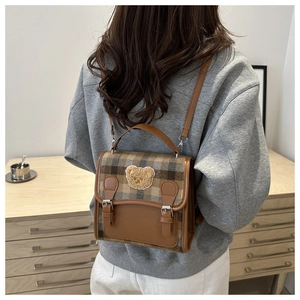 Rear view of a model wearing the brown plaid backpack with a plush bear patch and leather trim