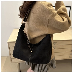 Détail du sac bandoulière en daim noir avec surpiqûres blanches et pompon sur un mannequin