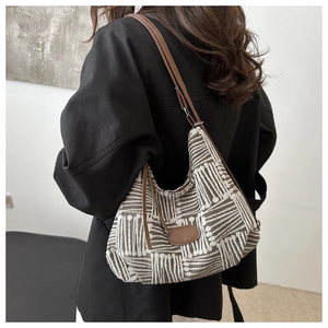 Detail view of large plaid fabric tote bag with brown leather strap worn by a model