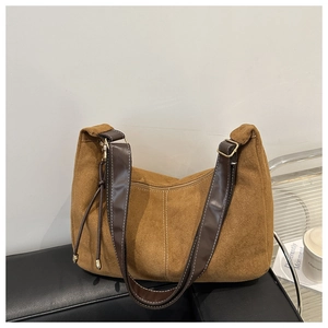 Détail du sac bandoulière en daim montrant des surpiqûres blanches et un gland à franges