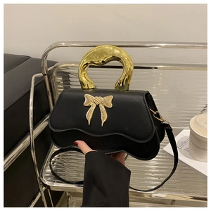 Detail of black leather handbag with golden bow ornament and metallic handle