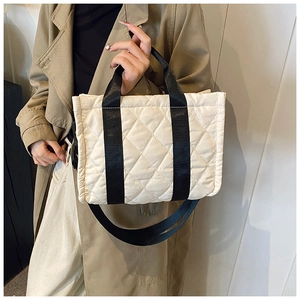 Close-up of beige quilted nylon tote bag with black straps and stitching details