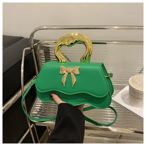 Detail of green crossbody bag with wavy flap, gold bow charm and unique metal handle