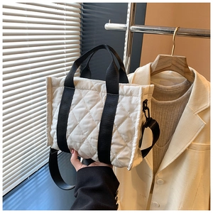 Detailed shot of white quilted tote bag with black straps in a minimalist indoor setting