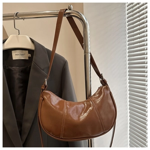 Detail of a brown glossy leather crescent hobo bag hanging on a minimalist silver hanger
