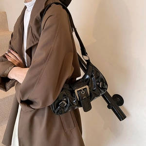 Glossy black shoulder bag with metal buckle and pleats shown on a model