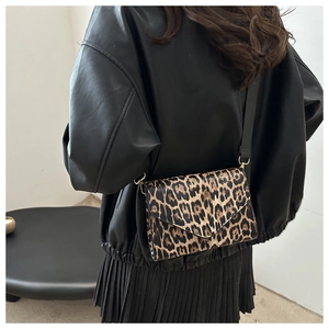 Détail du sac bandoulière à motif léopard avec boucles dorées porté par un mannequin