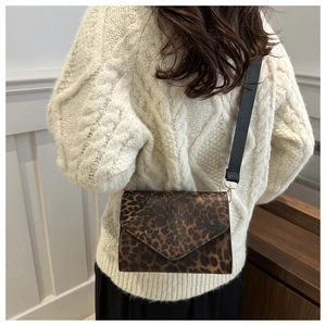 Détail du sac bandoulière léopard avec large sangle noire sur un pull en maille beige