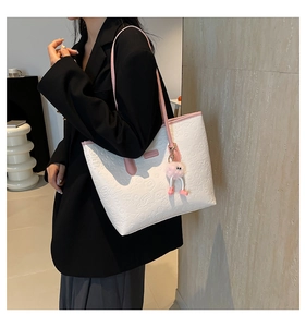 Detail of white embossed tote bag with pink straps and a fuzzy charm on the side