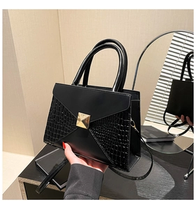 Detail of black faux crocodile leather handbag with golden square buckle and adjustable strap