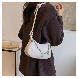 Detail of white half-moon bag featuring silver chain, pearl charm, and knotted leather strap