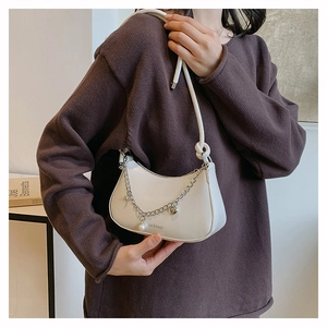 Detail of cream half-moon shoulder bag with metal chains, pearls, and heart charms