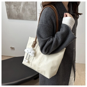 Detail of large beige leather tote bag featuring brown straps and soft cloud pendant