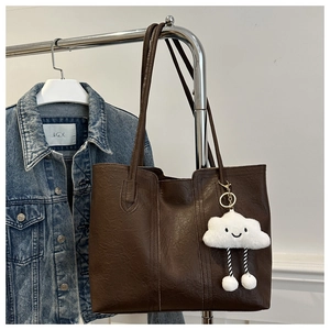 Detail of dark brown tote bag with plush cloud charm hanging on a metal rack