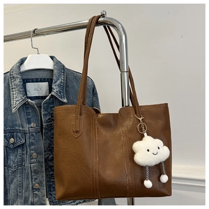 Detailed view of a brown faux leather tote bag with a cute white plush cloud charm
