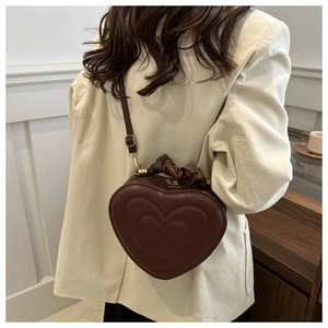 Detail of dark brown heart-shaped bag featuring embossed texture and cloud pleat handle