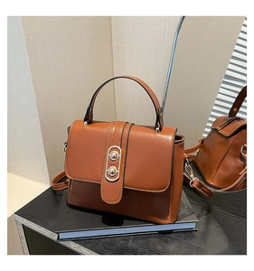 Detailed view of caramel brown leather handbag with gold metal clasp on a book base