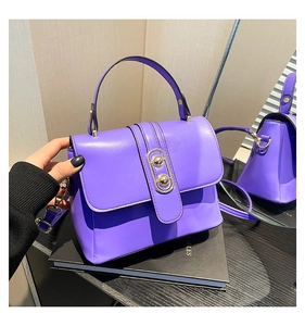 Detail of purple leather crossbody bag with distinctive gold sphere clasp and top handle