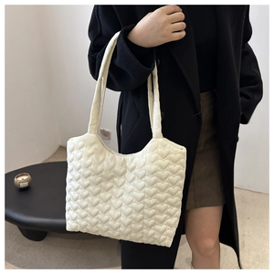 Detailed view of white heart-quilted puffer tote bag worn over a black winter coat