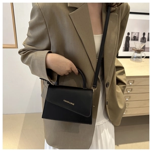 Detailed shot of mini black square bag with asymmetric flap and golden text accent