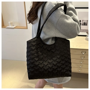 Detail of black quilted tote bag featuring heart pattern embroidery and padded strap