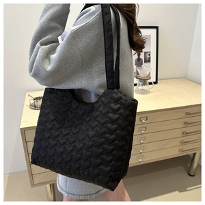 Detail view of black tote bag featuring puffy heart-quilted texture and soft double handles