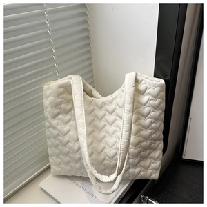Detail of white quilted tote bag featuring embossed heart patterns and padded shoulder strap
