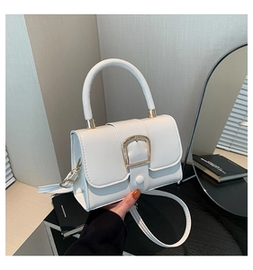 Close-up of white structured handbag featuring a large gold buckle and handle