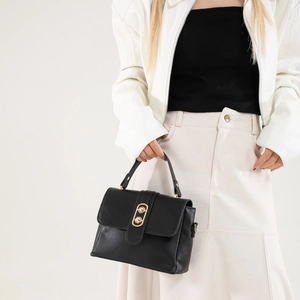 Elegant black faux leather crossbody handbag with gold buckle shown on a model