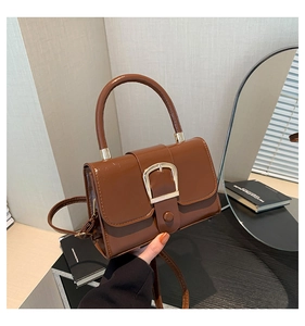 Detail of a brown glossy patent leather mini bag with a large gold U-shaped buckle