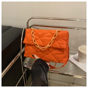 Détail d'un sac bandoulière matelassé orange avec texture bouffante et chaîne