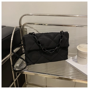 Detail of black quilted crossbody bag with chunky chain strap on a modern shelf