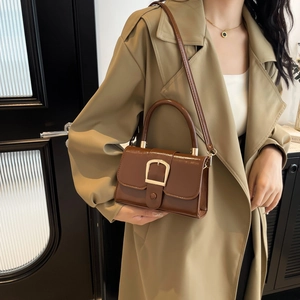Brown patent leather rectangular handbag with gold U-buckle and round handle in use