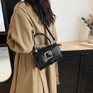 Glossy black square handbag with gold buckle shown on a model wearing a trench coat