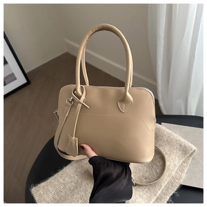 Close-up of beige leather tote bag with curved stitching and matching leather charm