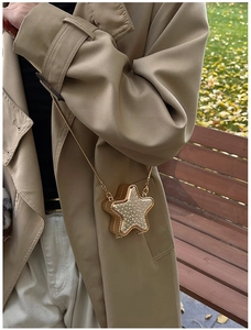 Close-up of star-shaped rhinestone mini bag with gold chain worn on a trench coat