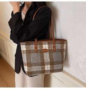 Close-up of brown and gray plaid wool tote bag featuring leather handles and gold rivets
