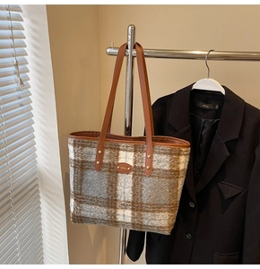Detail of wool plaid tote bag featuring brown leather handles and oval metal logo plate